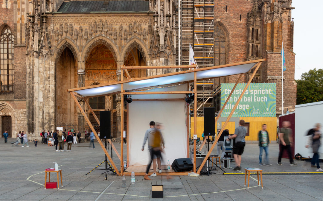 Die mobile Bühne "Qube" bei der Ulmer Kulturnacht. Das asymmetrische Holzgestell mit weißem Stoffdach ist vor dem Ulmer Münster aufgebaut. | Bild: Luca Linder