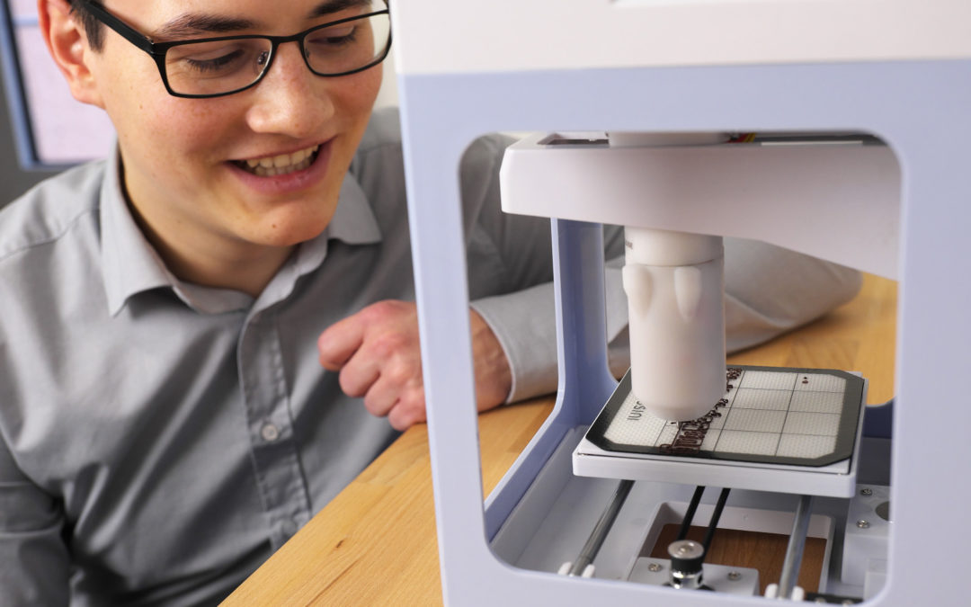 Ein Mann mit Brille betrachtet einen 3D-Drucker der gerade druckt